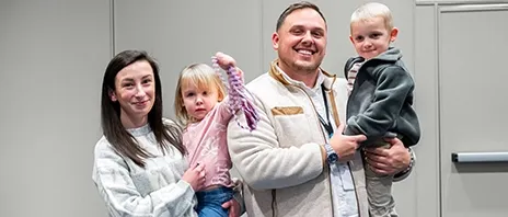 Kara DeBaker, her husband, and two kids smile at the camera.